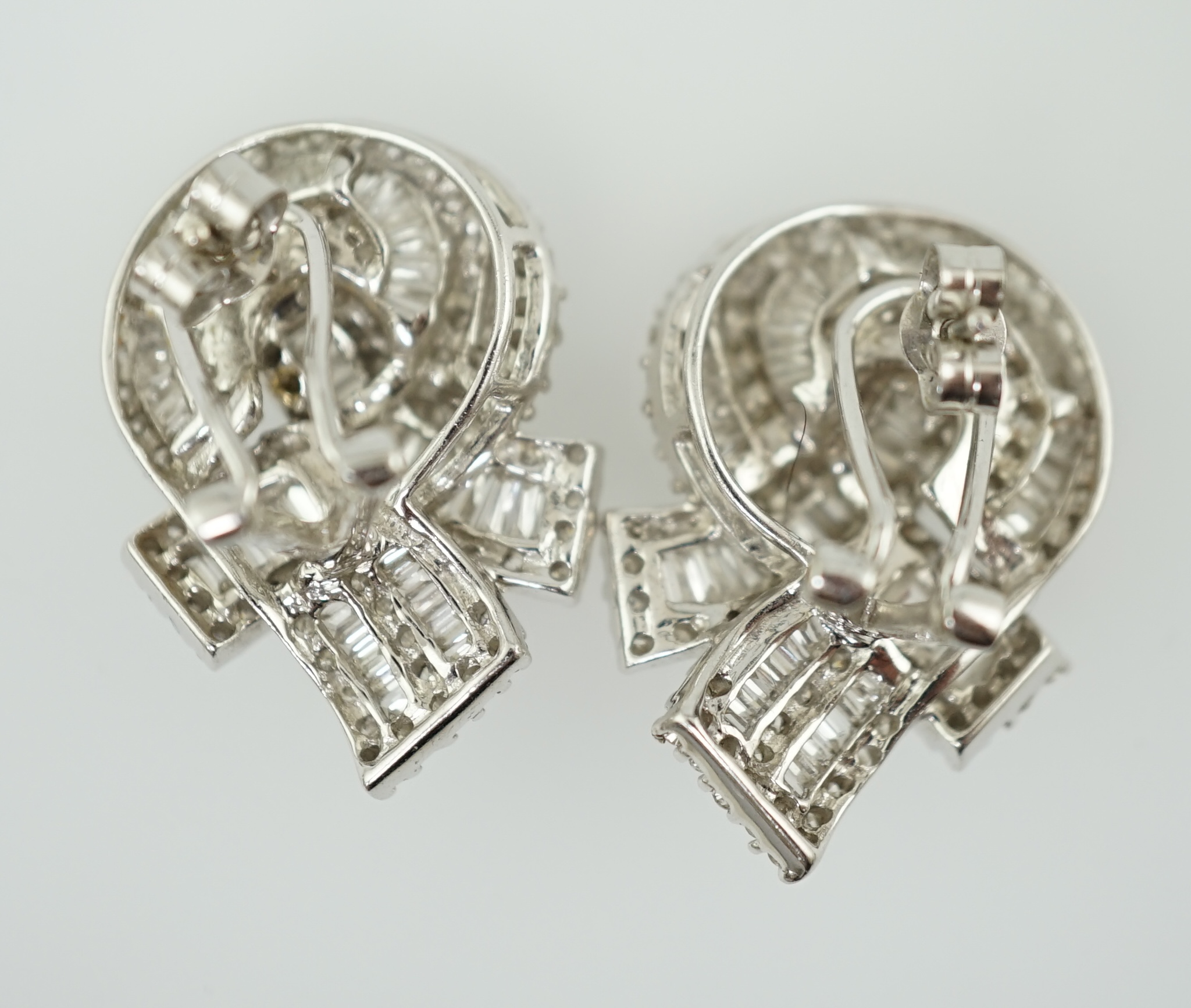 A pair of 18k white gold and pave set round and baguette cut diamond cluster set 'knot' earrings